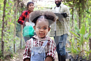 Portrait of cute litter African American girl with curly hair working in farm together with parents, child smiling with mother and