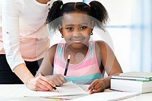 Portrait of cute little african student doing homework with caucasian teacher.