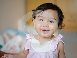 Portrait of a cute little Asian babe who is happy sitting in bed smiling, mouth smeared with food and looking at the camera. baby
