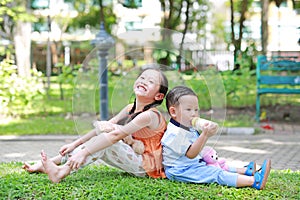 Portrait of cute little Asian sister and her younger brother sit back and lean back together in the green garden. Child girl