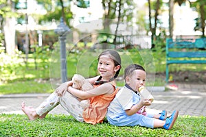 Portrait of cute little Asian sister and her younger brother sit back and lean back together in the green garden. Child girl