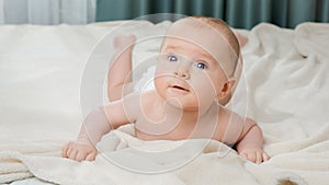Portrait of cute little baby boy with blue eyes lying on white blanket in bedroom
