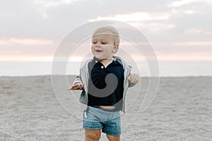 Portrait of Cute Little Baby Boy Child Playing and Exploring in the Sand at the Beach During Sunset Outside on Vacation in Hoodie