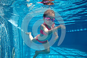 Portrait of cute little baby girl, toddler in pink swimsuit and goggles diving, swimming underwater in swimming pool
