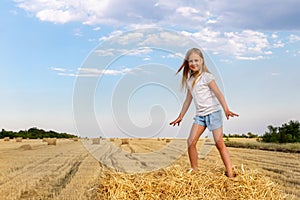 Portrait of cute little blond beautiful adorable cheerful caucasian kid girl enjoy sitting on hay stack or bale on