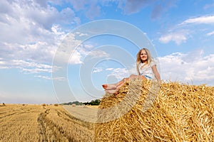 Portrait of cute little blond beautiful adorable cheerful caucasian kid girl enjoy sitting on hay stack or bale on