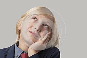 Portrait of a cute little boy with blond hair and blue eyes in a blue jacket and red tie on a gray background