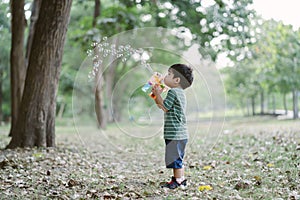 Portrait of Cute little boy blowing bubbles with gun that blows soap bubbles in the park at the day time. Kid plays with soap