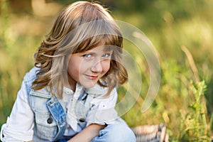 A portrait of a cute little boy with blue eyes and long blond hair sitting on a basket outside at sunset