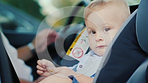 Portrait of a cute little boy boy, sits in a children`s car seat near the pope. Safety and child care concept