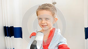 Portrait of cute little boy drying his wet hair with hairdryer after taking bath