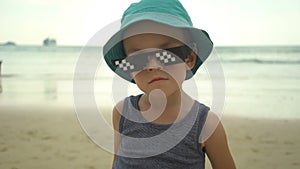 Portrait of cute little boy in straw hat with sunglasses standing on summer beach.