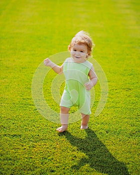 Portrait of cute little caucasian baby child having fun in garden. Little kid crawling on green grass lawn during walk