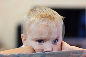 The portrait of cute little caucasian boy with light golden hair and blue eyes, with melancholy impression, propping up his head.