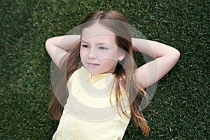 Portrait of a cute little caucasian girl lying on a green grass, resting in park on a summer day