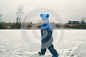 Portrait of cute little child boy in blue knitted hat running on frozen pond. Winter activity outdoor