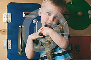 Portrait of cute little child boy hugging toy dinosaur on busyboard background. Kid in kindergarten, nursery  infant school or