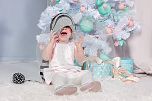 Portrait of cute little crying Princess girl in beautiful dress and striped hat sitting in studio decorated in christmas theme