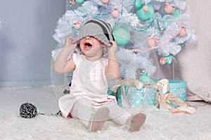 Portrait of cute little crying Princess girl in beautiful dress and striped hat sitting in studio decorated in christmas theme