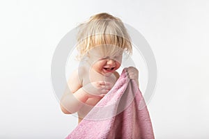 Portrait of a cute little curly girl covers her face with a terry towel, crying afraid to wash. childcare concept