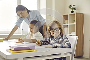 Portrait of cute little elementary student in glasses sitting at his desk in classroom
