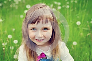 Portrait of cute little girl with beautiful smile and blue eyes sitting on the flower meadow, happy childhood