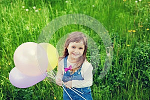 Portrait of cute little girl with beautiful smile holding toy balloons in hand on the flower meadow, happy childhood