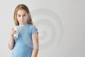 Portrait of cute little girl with blond long hair and blue eyes looking in camera with milk mustache and funny face