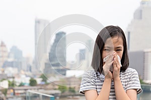 Portrait of cute little girl blowing nose in paper handkerchief,Asian child sneezing in a tissue in the city building as