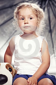 Portrait of a cute little girl in casual dress sitting with a plush toy in studio.