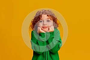 Portrait of cute little girl, child with curly red hair posing isolated over yellow background. Angel face