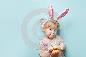 Portrait of a cute little girl dressed in Easter bunny ears holding colorful egg on blue background