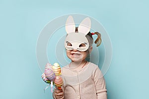 Portrait of a cute little girl dressed in Easter bunny ears holding colorful egg on blue background
