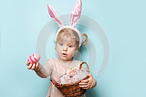 Portrait of a cute little girl dressed in Easter bunny ears holding colorful eggs on blue background