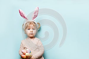 Portrait of a cute little girl dressed in Easter bunny ears holding colorful eggs on blue background