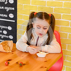Portrait of a cute little girl eating french fries in a fast food restaurant.