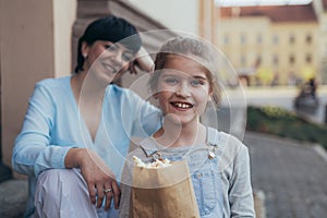 Portrait of cute little girl holding popcorn in city, mother in blurred background