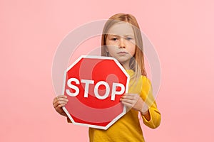 Portrait of cute little girl holding Stop symbol, red traffic sign and looking with serious responsible expression