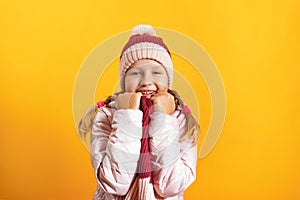 Portrait of a cute little girl in a jacket, scarf and hat on a yellow background. Autumn and winter concept