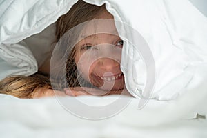 Portrait of a cute little girl laughing and hiding under the blanket.