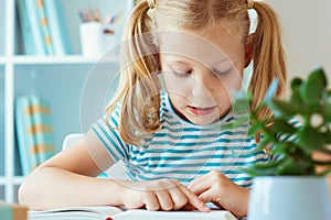 Portrait of a cute little girl read book at the table in classroom