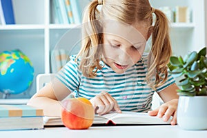 Portrait of a cute little girl read book at the table in classroom