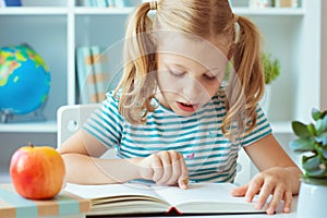 Portrait of a cute little girl read book at the table in classroom