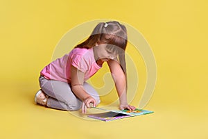 Portrait of cute little girl reading book on light background