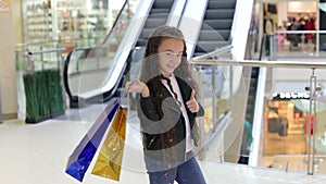 Portrait of a cute little girl in a shopping mall with package with thumb up.