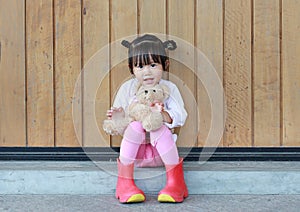 Portrait of cute little girl sit and hugging Teddy Bear against wood plank wall
