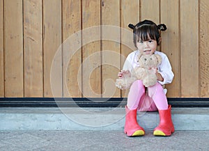 Portrait of cute little girl sit and hugging Teddy Bear against wood plank wall