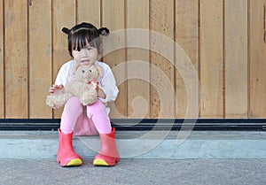 Portrait of cute little girl sit and hugging Teddy Bear against wood plank wall