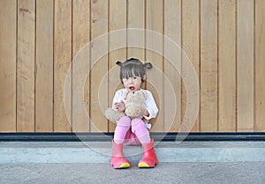 Portrait of cute little girl sit and hugging Teddy Bear against wood plank wall