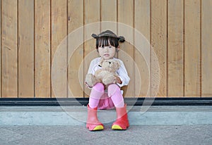 Portrait of cute little girl sit and hugging Teddy Bear against wood plank wall